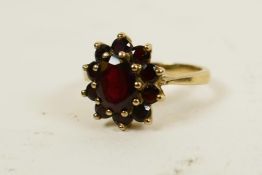 A 9ct gold and garnet dress ring set with central oval stone surrounded by ten small, round