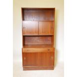 A mid-century teak bookcase with sliding doors and single drawer, split square handles and plinth