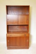 A mid-century teak bookcase with sliding doors and single drawer, split square handles and plinth