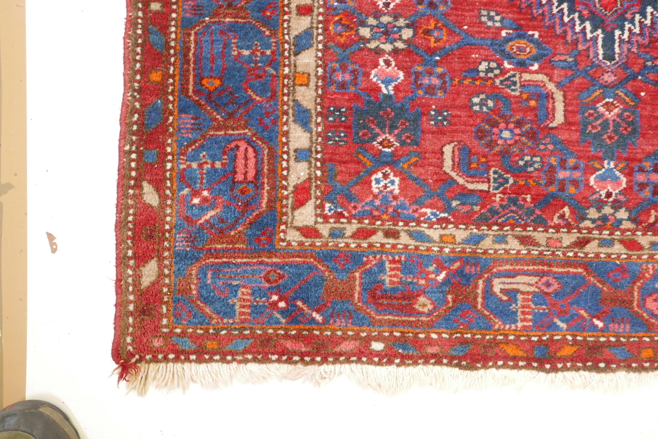 A Persian red ground wool carpet with a centralised medallion design on a blue border, 52" x 80" - Image 3 of 4