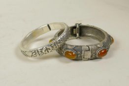 A Chinese white metal bangle decorated with the emblems of the eight Immortals, and another