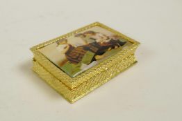 A gold plated metal pill box with an inset cold enamel plaque to the lid depicting children, 2" x