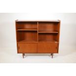A teak open bookcase with adjustable shelves and two cupboards with sliding doors, raised on