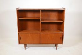 A teak open bookcase with adjustable shelves and two cupboards with sliding doors, raised on