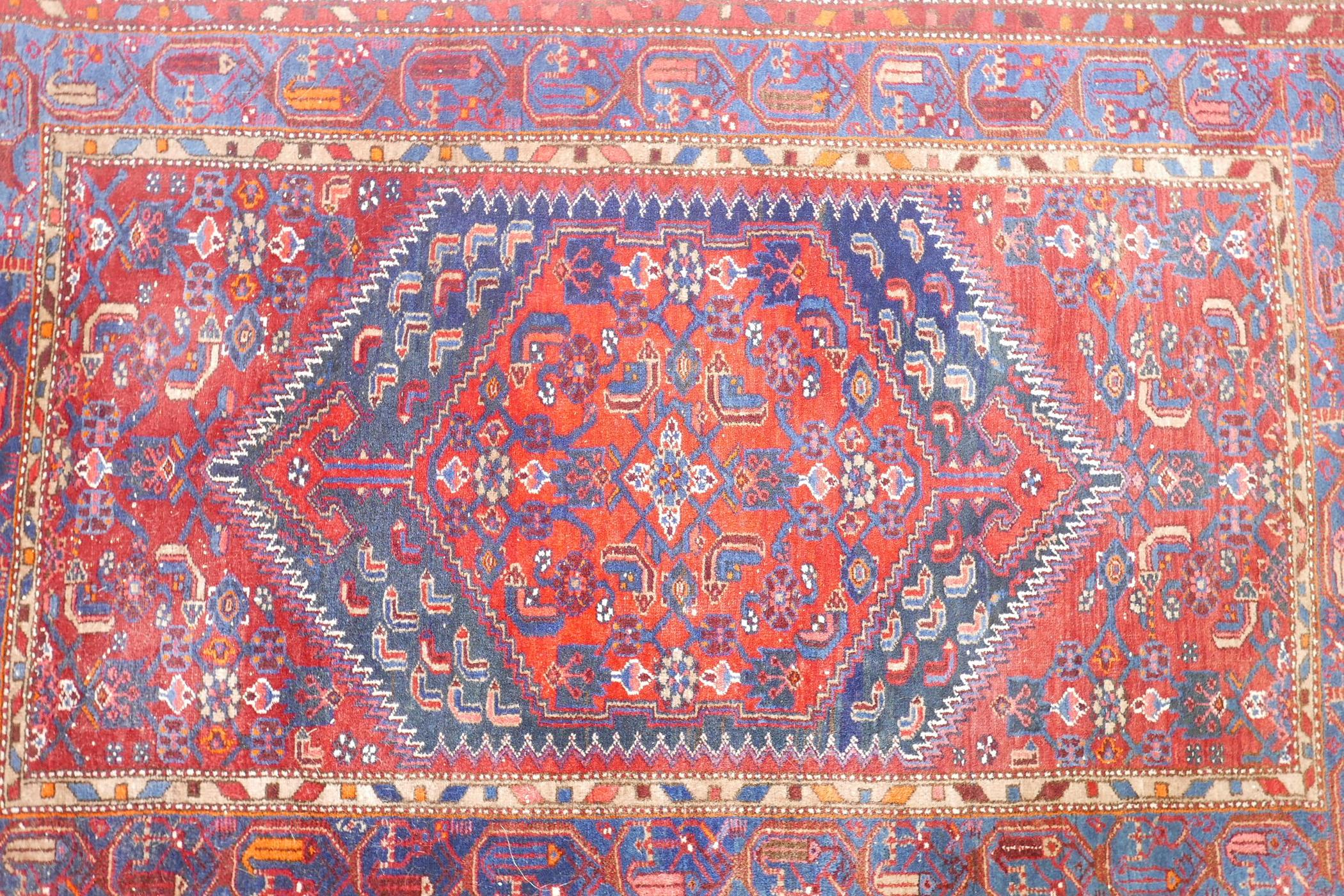 A Persian red ground wool carpet with a centralised medallion design on a blue border, 52" x 80" - Image 2 of 4