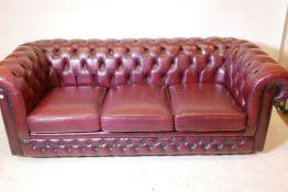 A Thomas Lloyd button back leather chesterfield with brass stud detail and ox blood covers, 78" wide