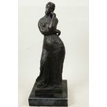 A bronze sculpture of a girl in a long dress standing in a pensive pose on a square marbled base,