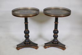 A pair of tilt top ebonised and parcel gilt lamp tables, with hand painted tops and pierced brass