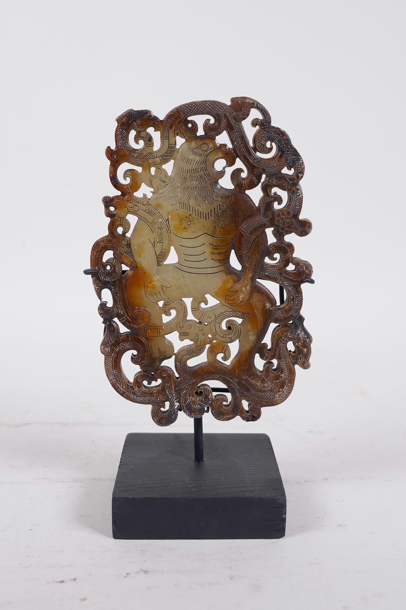 A Chinese pierced jade ornament, carved in the form of a bird headed man entwined with dragons, on a