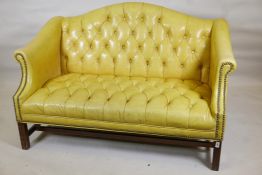 A Chippendale style buttoned leather two seater settee with brass studs and carved back and scroll