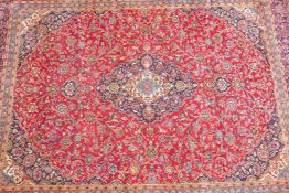 A large red ground full pile Persian Kashan carpet with a traditonal, multicoloured Kashan design,