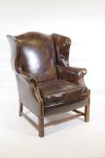 A Georgian style leather wingback armchair, with brass stud decoration, raised on square moulded