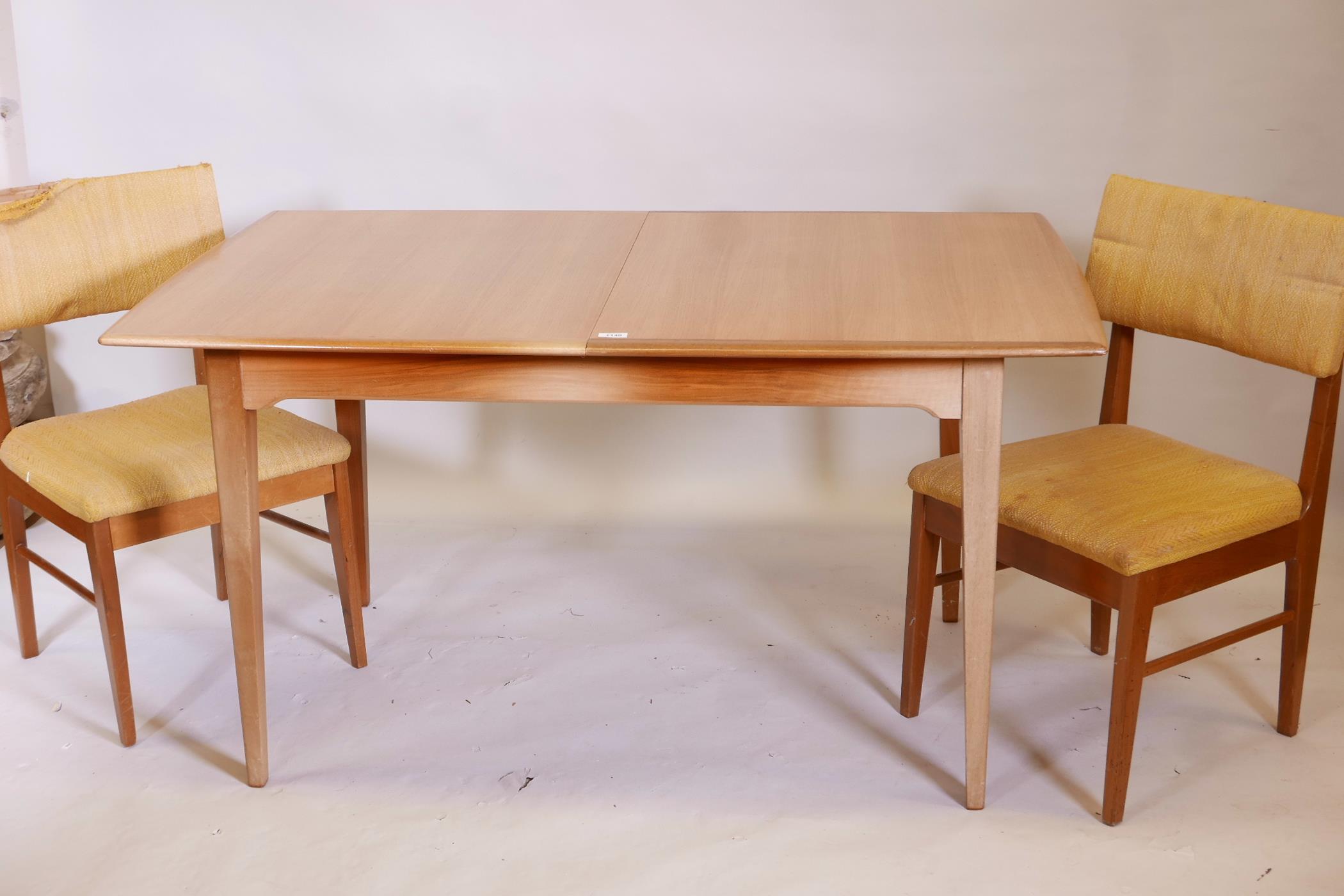 A 1970s teak extending dining table on square tapering supports, with built in leaf, and two