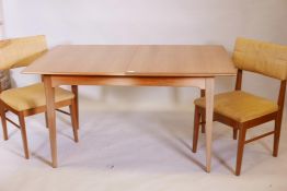 A 1970s teak extending dining table on square tapering supports, with built in leaf, and two