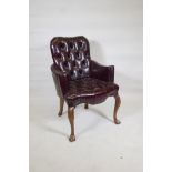 A Georgian style armchair with buttoned leather upholstery and scroll arms, raised on cabriole