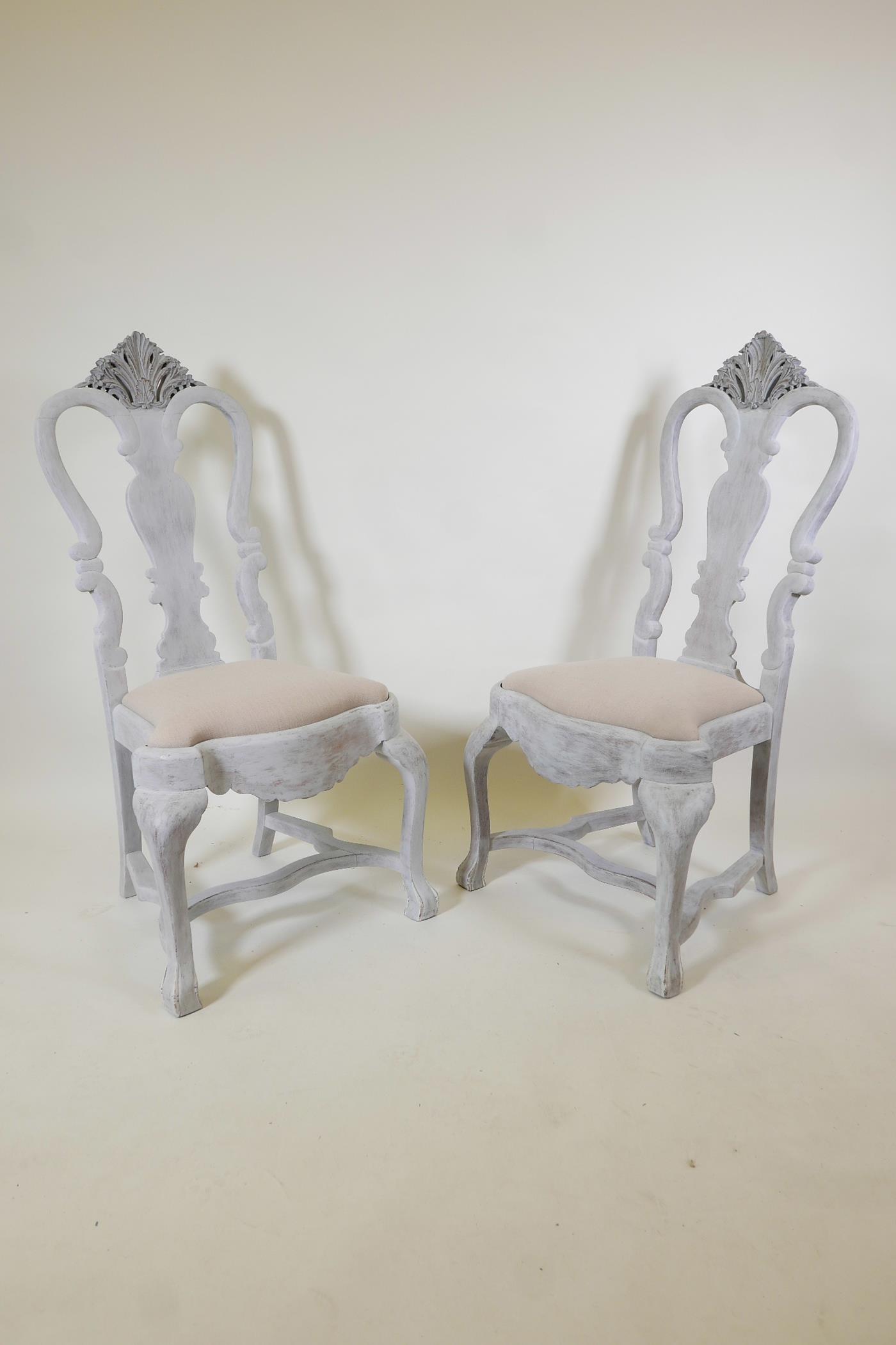 A pair of early C20th Gustavian style painted and distressed chairs, with carved details, 45" high