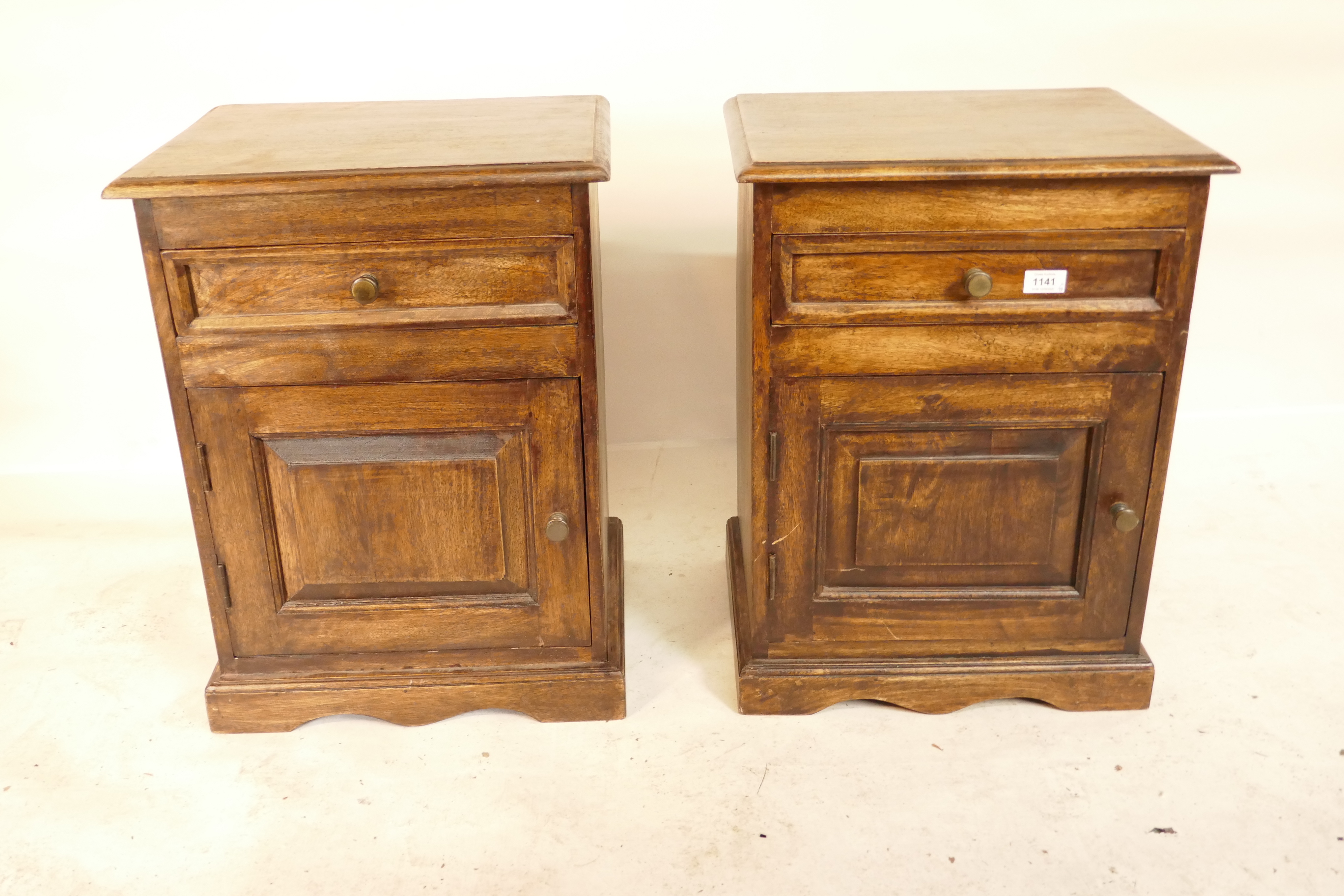 A pair of hardwood bedside cabinets with a single drawer over a door, raised on a plinth base,