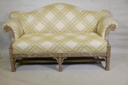 A camel back settee with scroll arms and carved and pierced frame, raised on square supports with