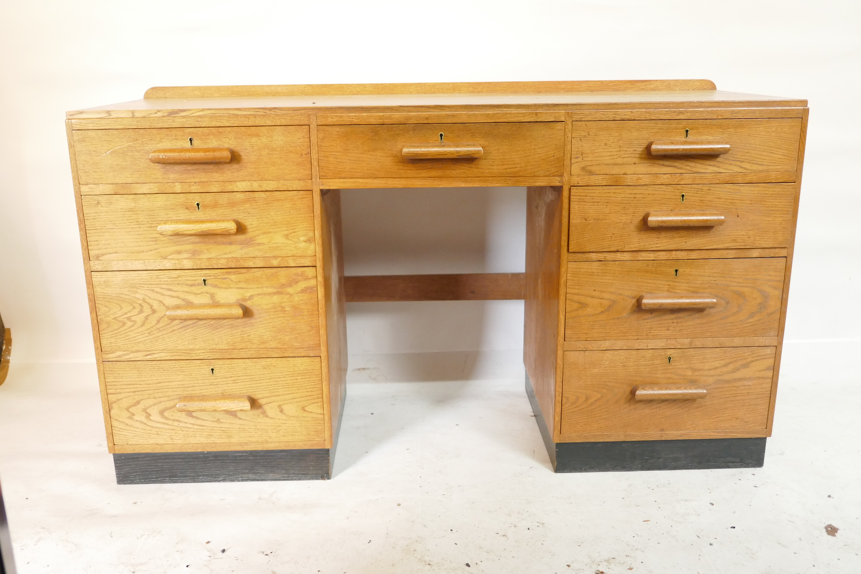 An Art Deco oak nine drawer kneehole desk, raised on a painted plinth, 54" x 18" x 30"