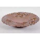 A beaten copper pedestal fruit dish with embossed apple, pear and grape decoration, 10¾" diameter