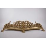 A brass fire fender of serpentine form, pierced with scrolls and winged putti, raised on paw feet,