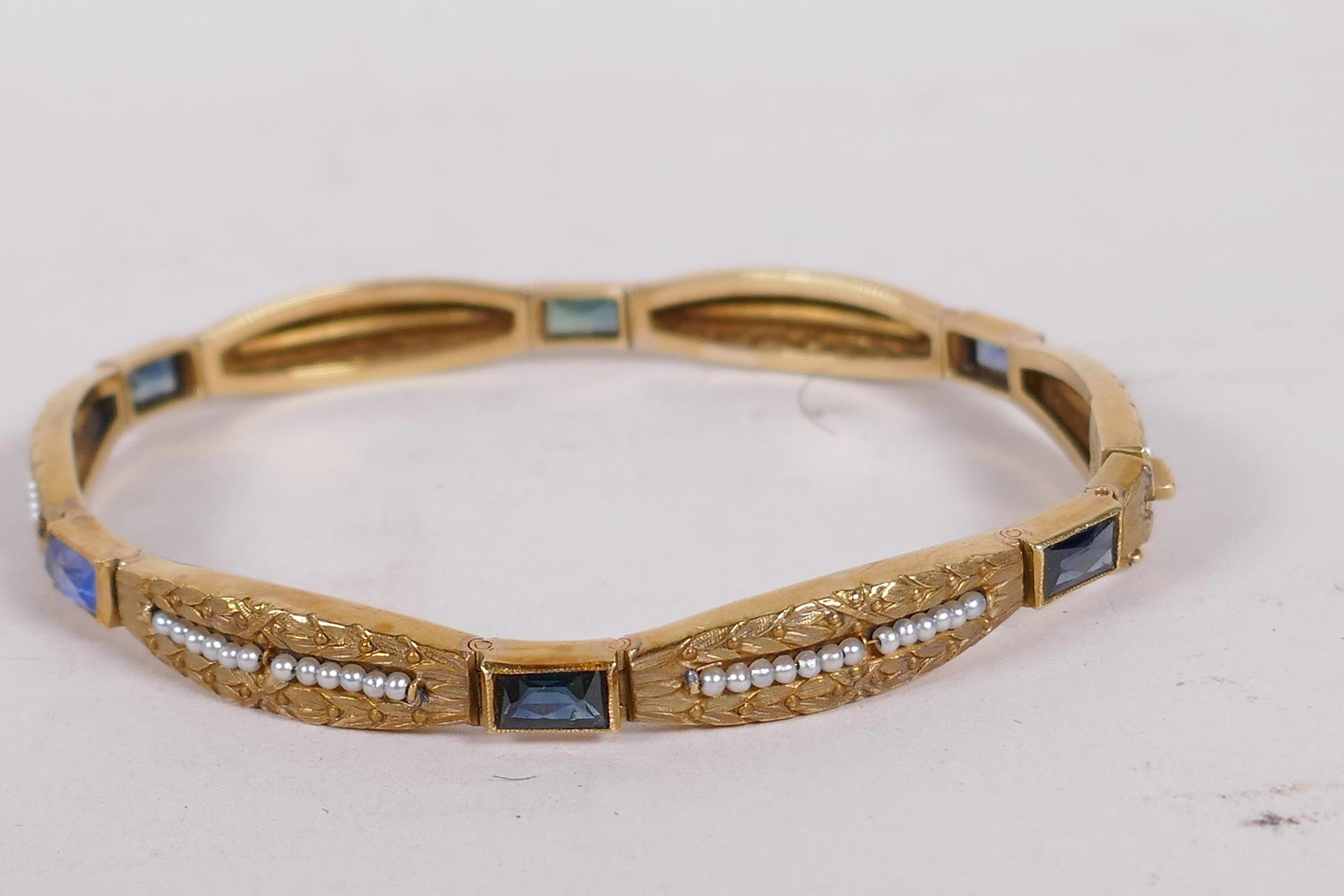 An 18ct gold bangle set with sapphires and seed pearls, and having bark finish engraving (15 grams