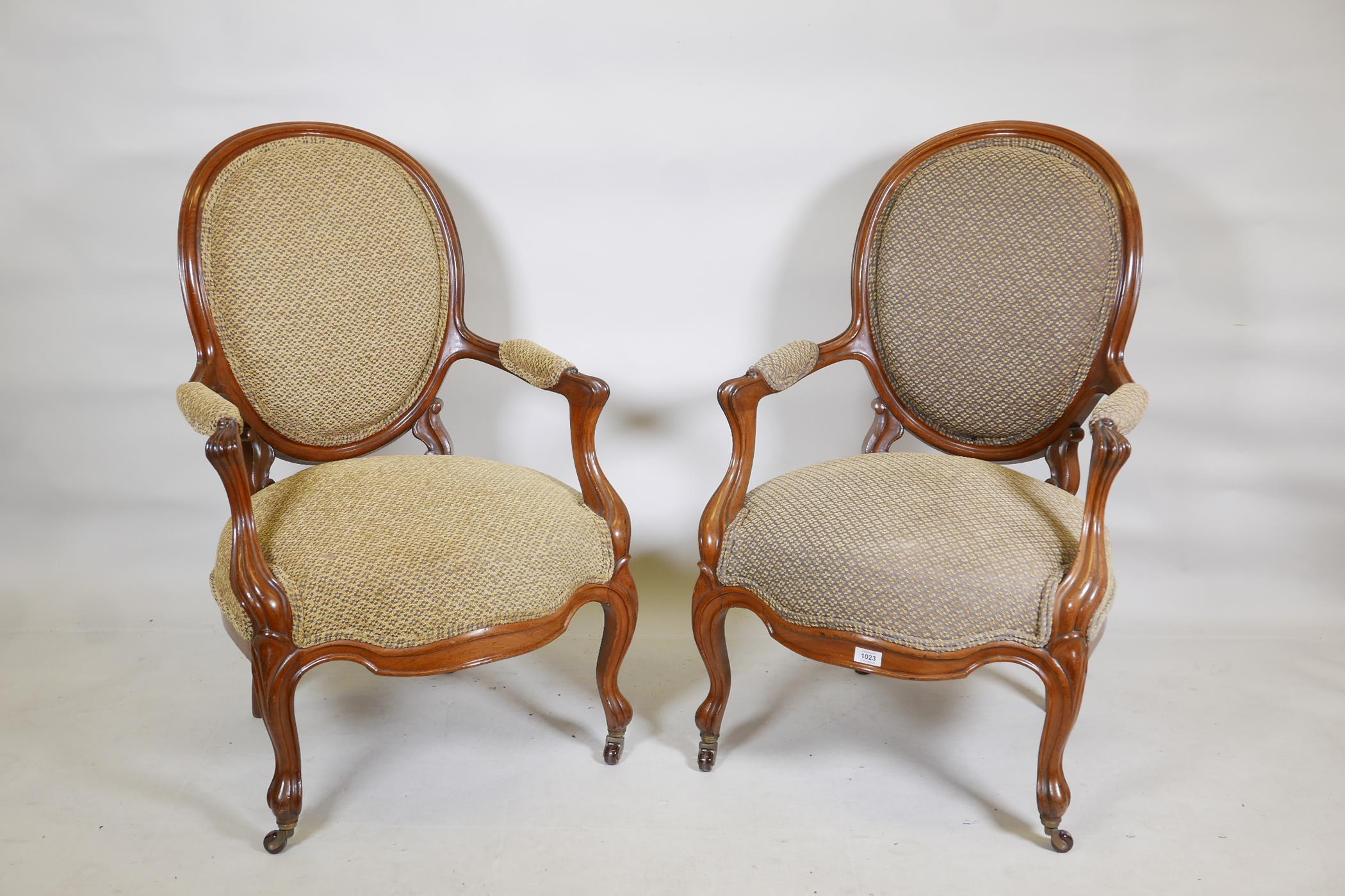 A pair of walnut spoonback open armchairs with carved and shaped arms, raised on cabriole supports