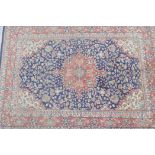 A red ground Persian wool rug with a traditional Kashan style blue medallion design, 60" x 83"