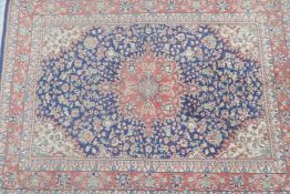 A red ground Persian wool rug with a traditional Kashan style blue medallion design, 60" x 83"