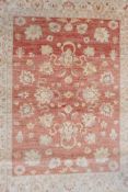 A Pakistani washed red ground wool rug with a floral design and cream borders, 61" x 80"