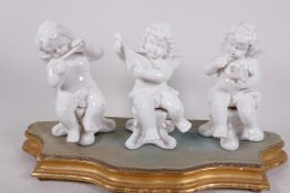 A set of three Continental porcelain figures of cherub musicians, 6½" high, on a shaped gilded stand