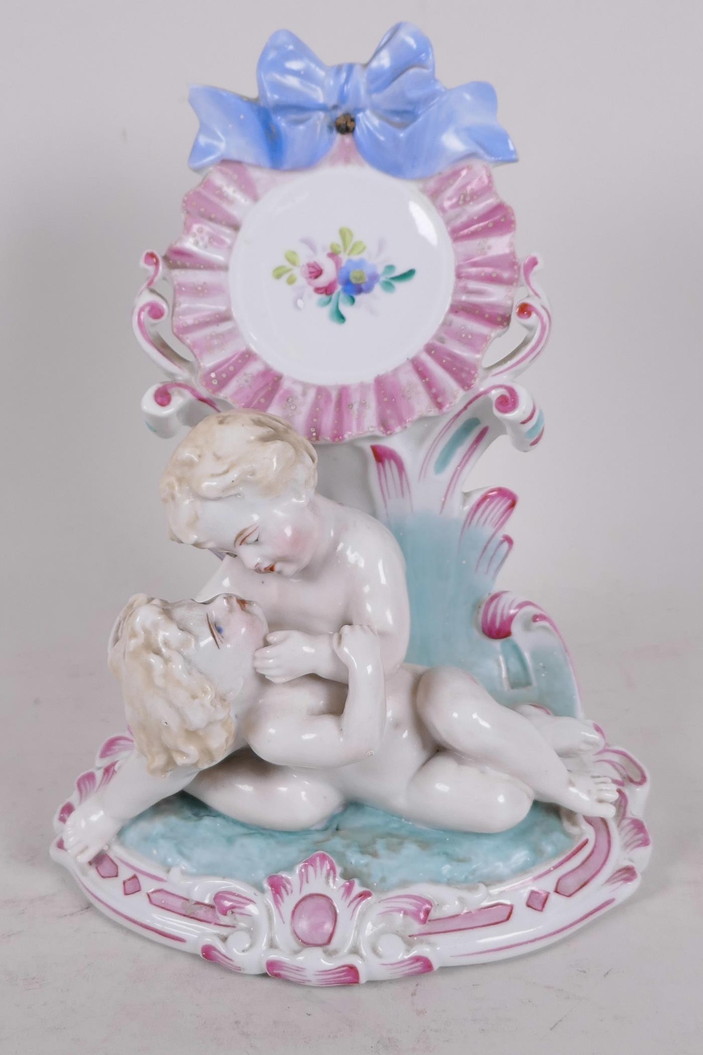 A C19th Continental porcelain watch holder formed as two children in a garden hand painted with