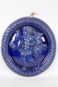 A dark blue glazed Dunmore Pottery oval wall plaque embossed with a putti and doves, 12" x 11"