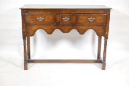 A Georgian style oak dresser base, with three drawers and shaped apron, raised on turned supports