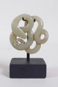 A Chinese carved and pierced celadon jade pendant in the form of an entwined snake, on a display