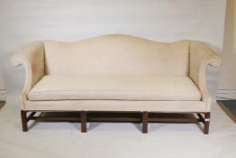 A Chippendale style camel back settee with scroll arms, raised on moulded chamfered supports