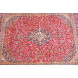 A large red ground full pile Persian Kashan carpet with a traditonal, multicoloured Kashan design,