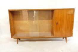 A mid C20th teak side cabinet with single door and two sliding glass doors, bears label Herbert E.