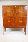 A mid century figured mahogany four door cabinet, each door inlaid with scenes of industry, the