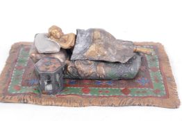 A cold painted bronze figure of a woman lying on a couch set on a Persian rug, the bed cover lifting