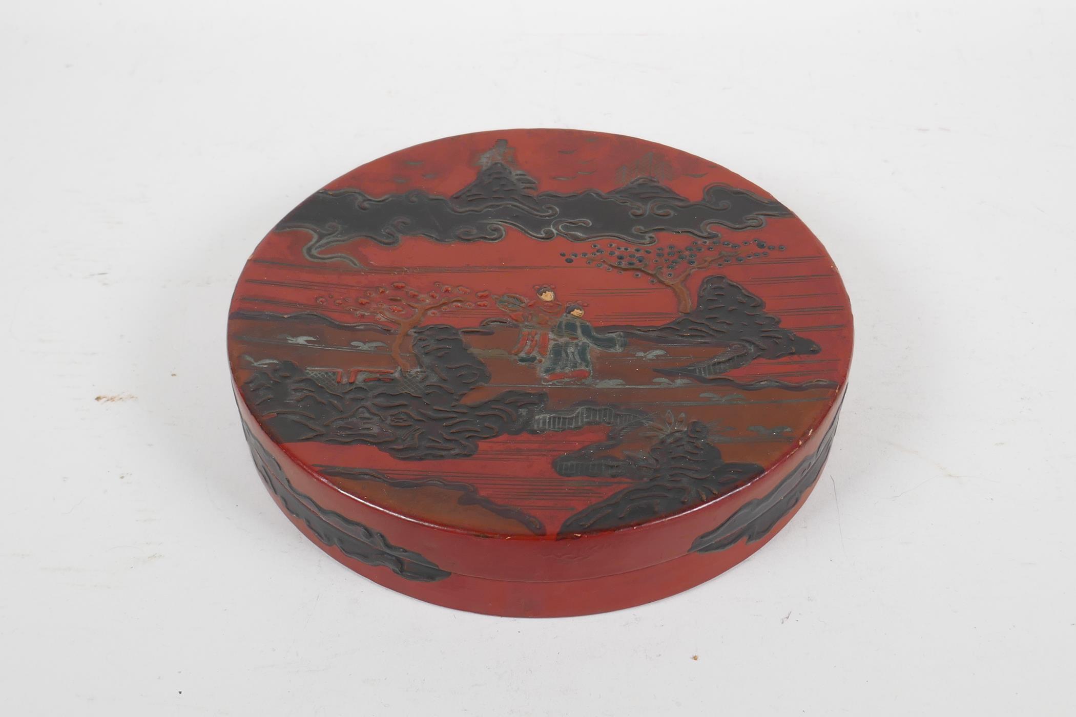 A Japanese red and black lacquer cylinder box decorated with figures in a landscape, the interior