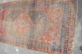 An Eastern tribal woven woolen rug with red ground and central medallion within three borders (