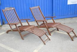 A pair of teak folding sun loungers with footrests