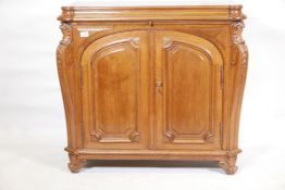 A C19th walnut side cabinet, with two moulded arched doors flanked by carved and shaped canted