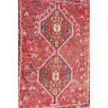 An Iranian red ground wool carpet decorated with twin geometric medallions on a floral patterned