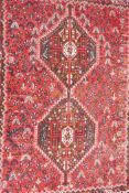 An Iranian red ground wool carpet decorated with twin geometric medallions on a floral patterned