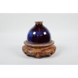 A Chinese porcelain water pot with a Jun ware flambe glaze, on a carved hardwood stand, 5" high