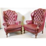 A pair of Georgian style leather wing back armchairs, with button backs and brass studs, raised on