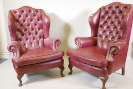 A pair of Georgian style leather wing back armchairs, with button backs and brass studs, raised on