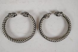 A pair of Chinese twisted white metal bangles with cast dragon's head ends, 2" diameter